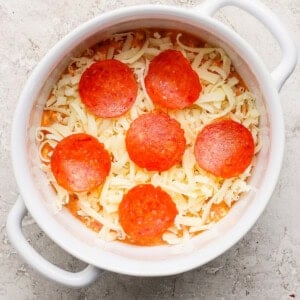 Egy kerek fehér étel, amely aprított sajtot és hat szelet pepperonit tartalmaz egy texturált felületen.