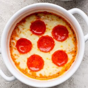 Sült edény, olvasztott sajttal és hat, egyenletesen elhelyezett pepperoni szeleten, fehér ramekin -ben egy texturált felületen.
