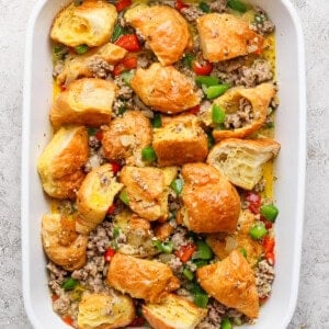 Baking dish with a casserole of browned bread pieces, ground meat, chopped green bell peppers, and diced red peppers.