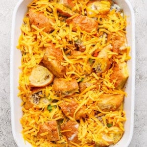 A white baking dish with baked bread cubes, sliced sausage, vegetables, and shredded cheese on top.