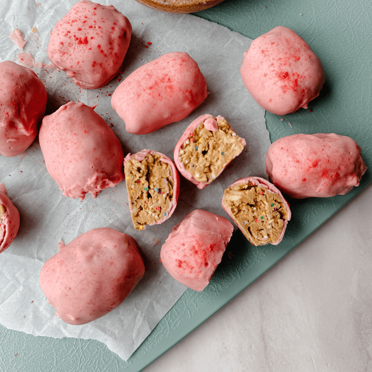 Pink-coated truffles on parchment, some sliced open to reveal a cake-batter-like filling with colorful sprinkles.