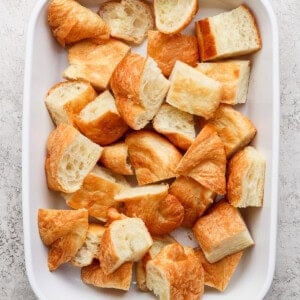 A white baking dish filled with bite-sized croissant pieces on a textured surface.