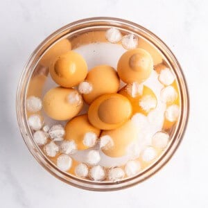A bowl of brown eggs is submerged in water with ice cubes, set against a white background.