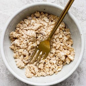 A bowl of dry oatmeal mixture with a gold fork placed inside on a textured surface.