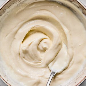 A bowl filled with smooth, creamy white yogurt being stirred with a metal spoon on a light surface.