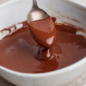 A spoon is dipped into a bowl of melted chocolate, with some chocolate coating the spoon.