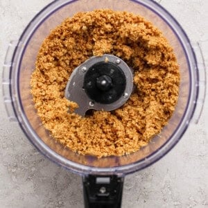 A food processor containing a mixture of finely ground ingredients on a light textured surface.