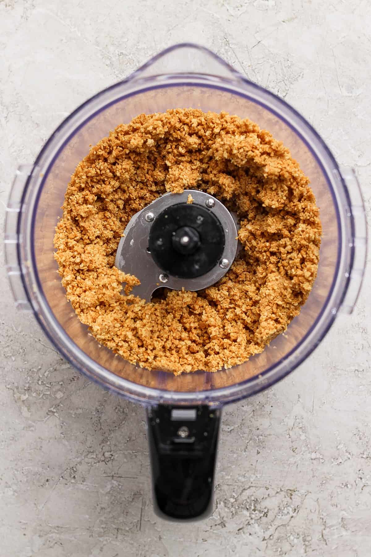 A food processor containing a mixture of finely ground ingredients on a light textured surface.