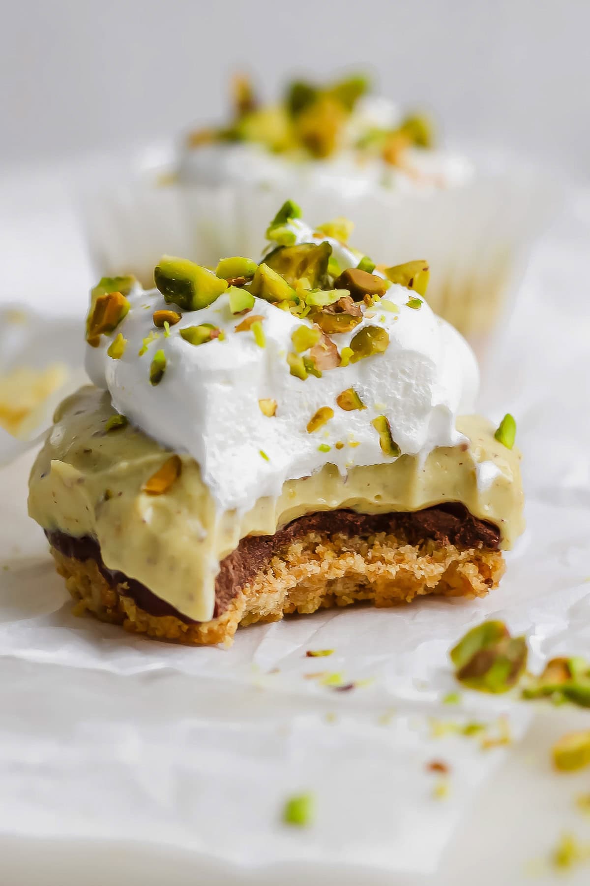 A close-up of a dessert with a crumbly base, creamy middle layer, whipped topping, and chopped pistachios, with a bite taken out of it.
