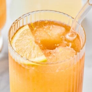 A close-up of an iced beverage in a ribbed glass, garnished with a lime wedge and served with a clear straw.