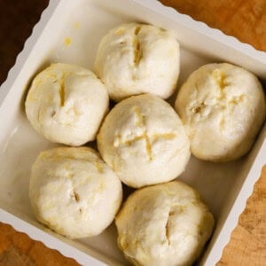 Six unbaked dough balls evenly arranged in a white baking dish, placed on a wooden surface.