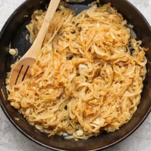 Sliced onions caramelizing in a black cast iron skillet with a wooden spoon resting on top.