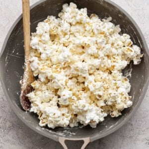 A pan filled with popcorn coated in a white, sticky mixture, with a wooden spoon resting on the side.
