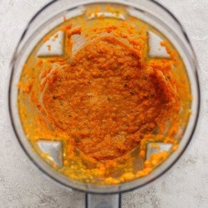 A blender with orange vegetable puree inside, viewed from above on a light-colored surface.