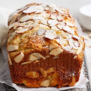 A loaf of almond bread inspired by cottage cheese pull apart bread, topped with sliced almonds and a dusting of powdered sugar, sits on parchment paper.