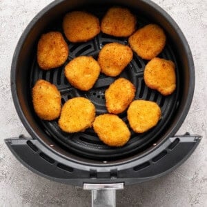 Chicken nuggets arranged in a single layer inside an air fryer basket on a light-colored surface.