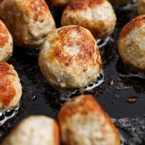 Close-up of several browned butter chicken meatballs cooking in a pan with visible bubbling oil.