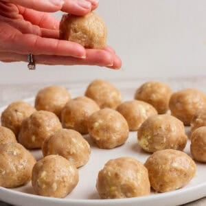 A person shapes a ball of dough for butter chicken meatballs over a plate filled with similar dough balls on a light-colored surface.