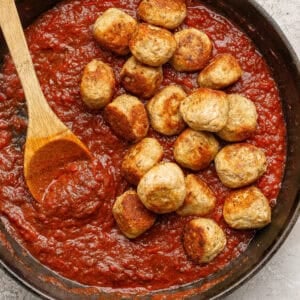 A cast iron skillet filled with rich tomato sauce and butter chicken meatballs, with a wooden spoon resting on the side.