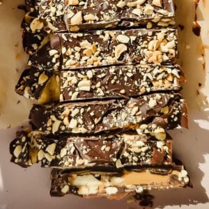 Rectangular pieces of chocolate bark topped with chopped nuts are arranged on a sheet of parchment paper.