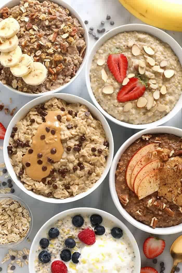 Different types of oatmeal in white bowls including chocolate chip peanut putter, strawberry, apple cinnamon, and high protein. 