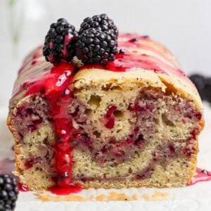 A loaf of blackberry bread with a slice cut, topped with blackberry sauce and fresh blackberries.