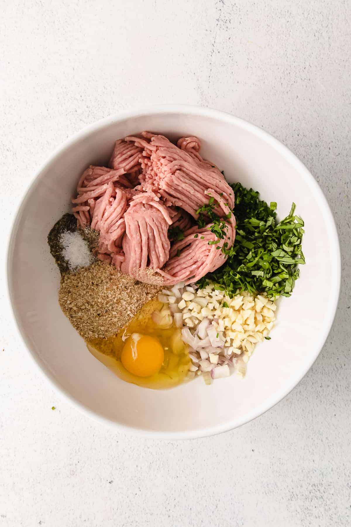Ingredients for meatballs in a white bowl.