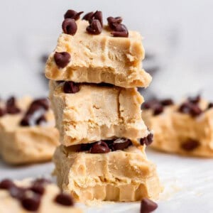 Three pieces of peanut butter fudge stacked on top of each other, each topped with chocolate chips, with more fudge pieces in the background.