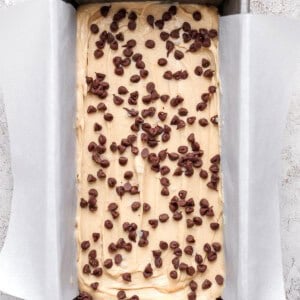 A rectangular metal loaf pan lined with parchment paper, filled with batter and topped with scattered chocolate chips, ready to be baked.