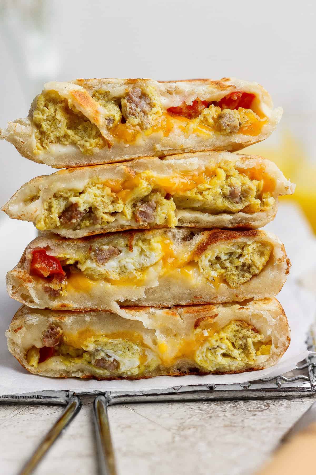 Four breakfast quesadilla wedges stacked on a cooling rack, filled with scrambled eggs, sausage, cheese, and pieces of tomato.