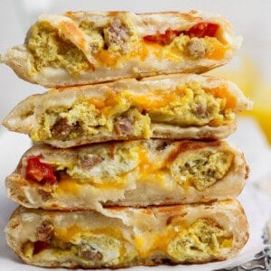 A stack of four breakfast quesadillas filled with scrambled eggs, sausage, cheese, and pieces of tomato, cut in half to show the fillings.