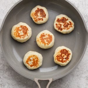 Six round, golden-brown patties are cooking in a nonstick skillet on a light-colored surface.