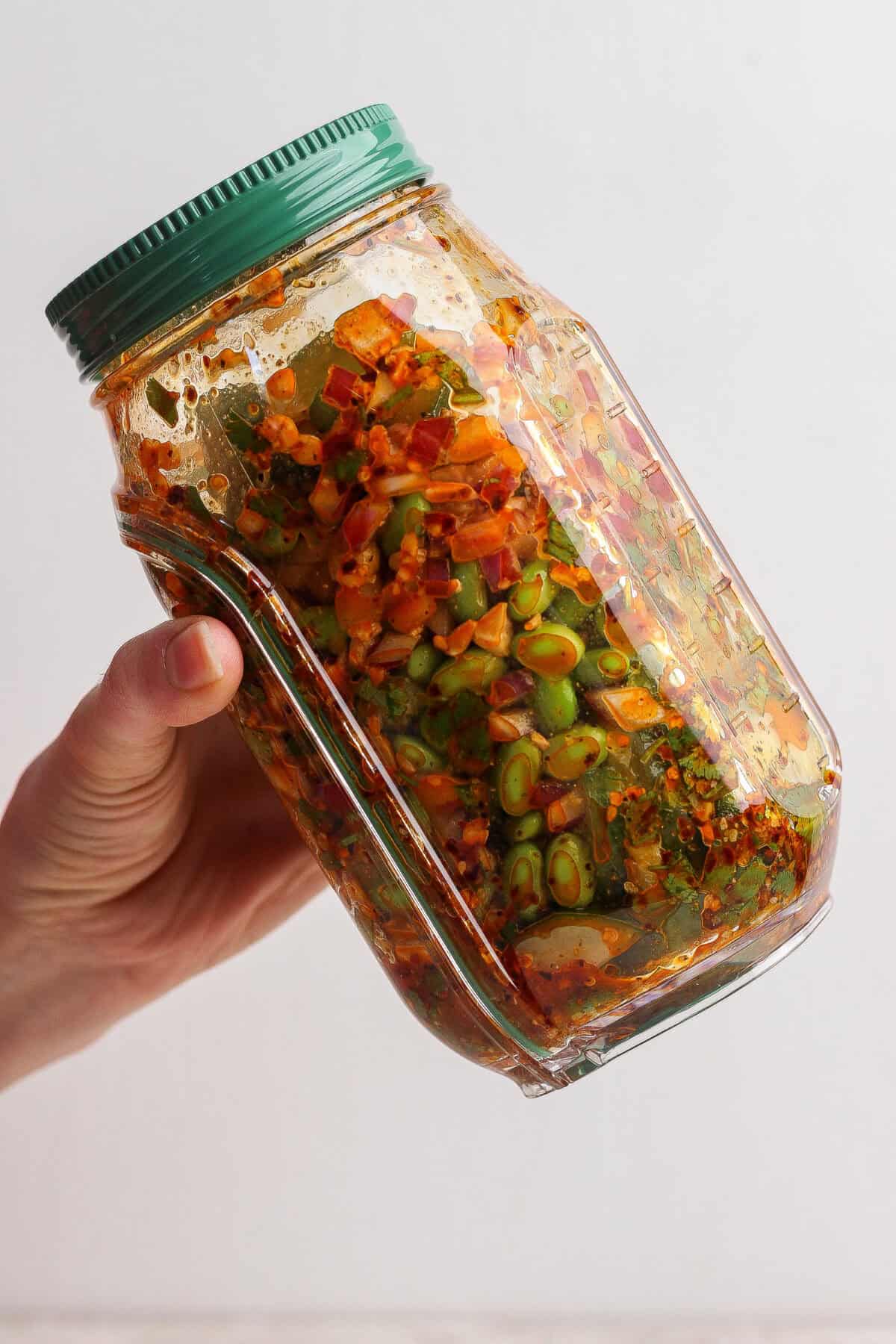 A hand holds a glass jar filled with colorful, chopped vegetables and spices, sealed with a green lid.