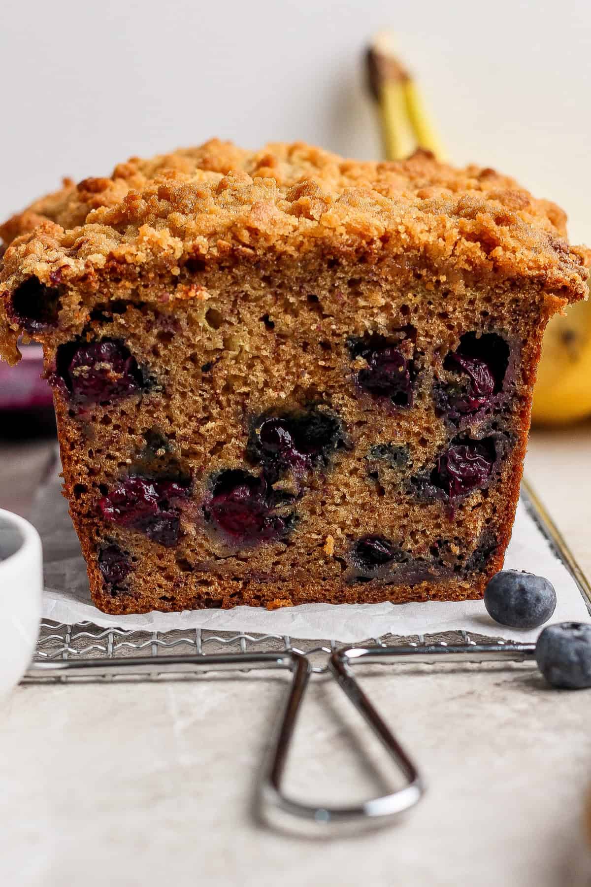 A close-up of a sliced loaf of blueberry banana bread with a crumb topping, showing blueberries inside the bread.
