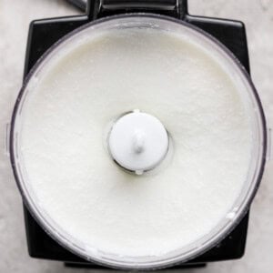 A food processor containing a smooth, white mixture viewed from above on a light-colored surface.