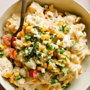 Bowl of pasta salad with corn, chopped red bell peppers, crumbled cheese, and fresh herbs, served with a fork.