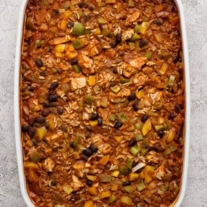 A white baking dish filled with a baked casserole containing rice, black beans, green peppers, and a tomato-based sauce.