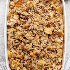 A rectangular baking dish filled with bread pudding topped with streusel and pecans, with a bowl of pecans and a cloth napkin nearby.