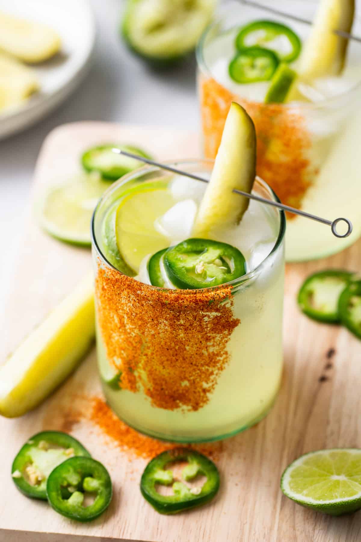 Two spicy pickle margaritas garnished with jalapeño and lime.