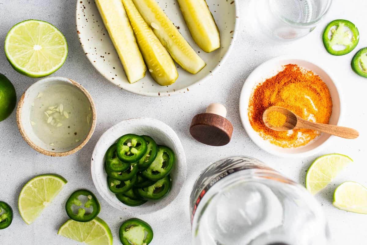 Spicy pickle margarita ingredients including jalapeños, limes, pickle juice, and tequila.