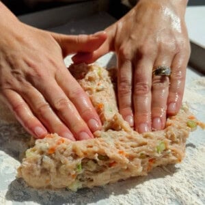 Pressing and shaping ground chicken protein bar mixture with vegetables on parchment paper
