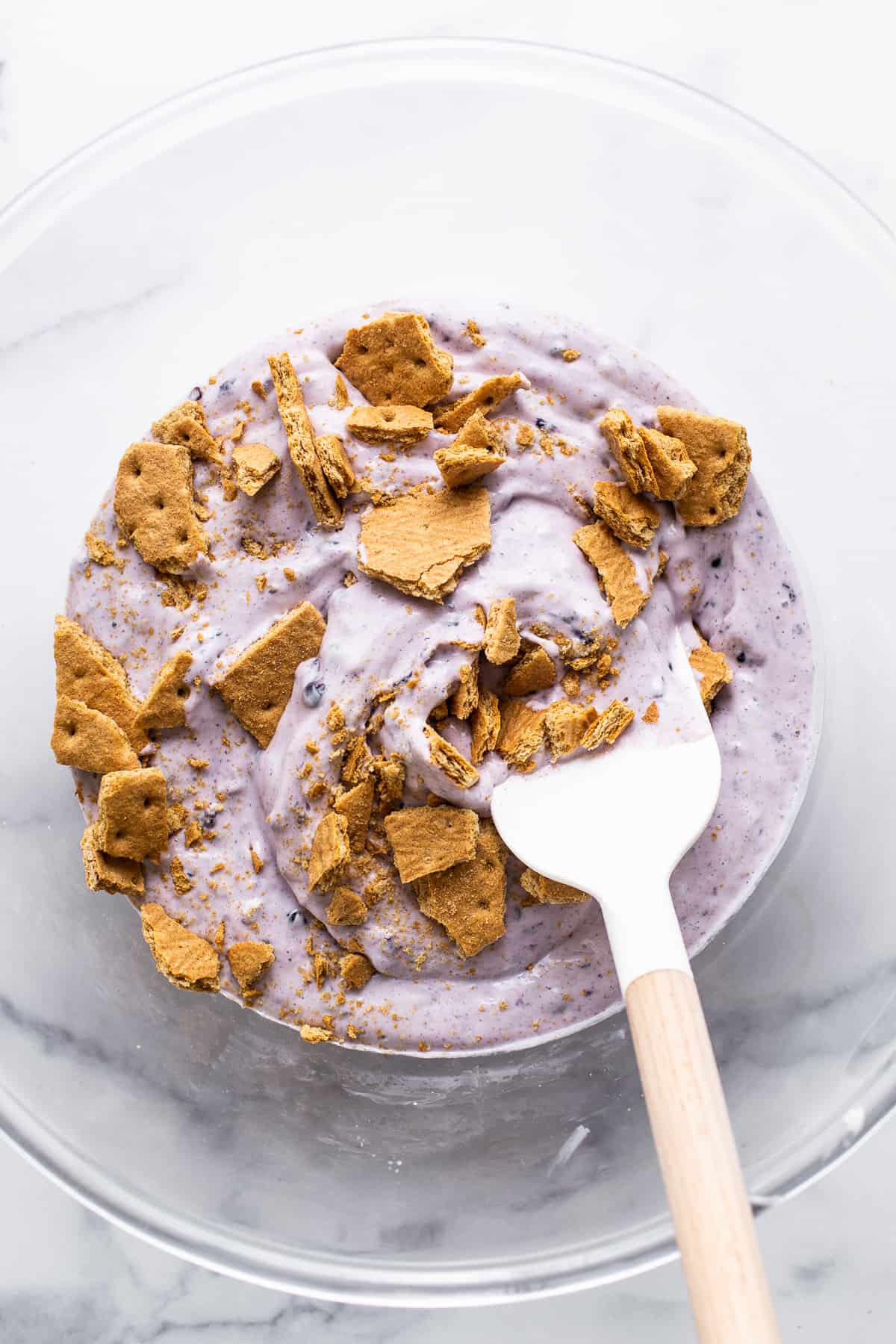 blackberry cottage cheese ice cream mixture in a mixing bowl with graham cracker crumbs.