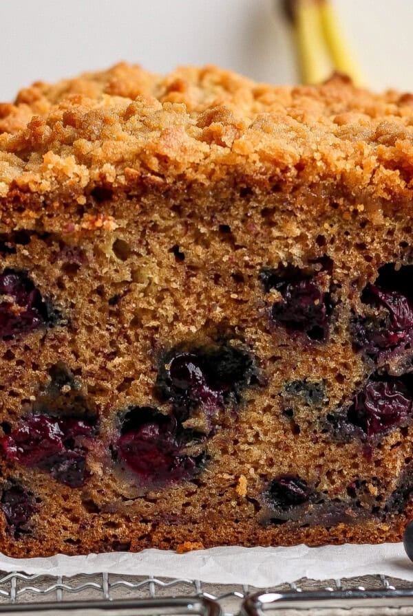 Close-up of a sliced loaf of blueberry banana bread with a crumbly topping, showing visible blueberries inside the moist bread.