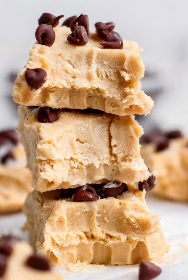 Three pieces of peanut butter fudge stacked on top of each other, each topped with chocolate chips, with more fudge pieces in the background.