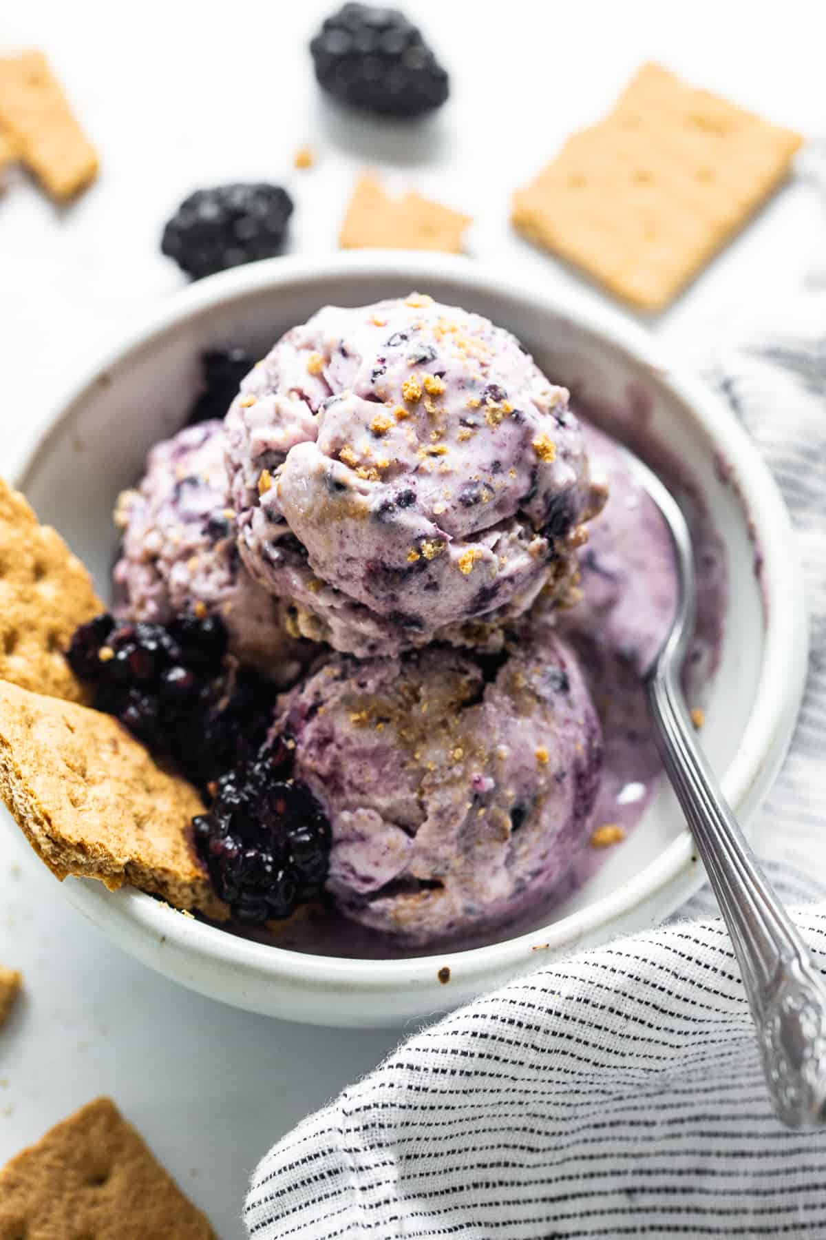 a scoop of blackberry cheesecake cottage cheese ice cream in a white bowl with fresh blackberries.
