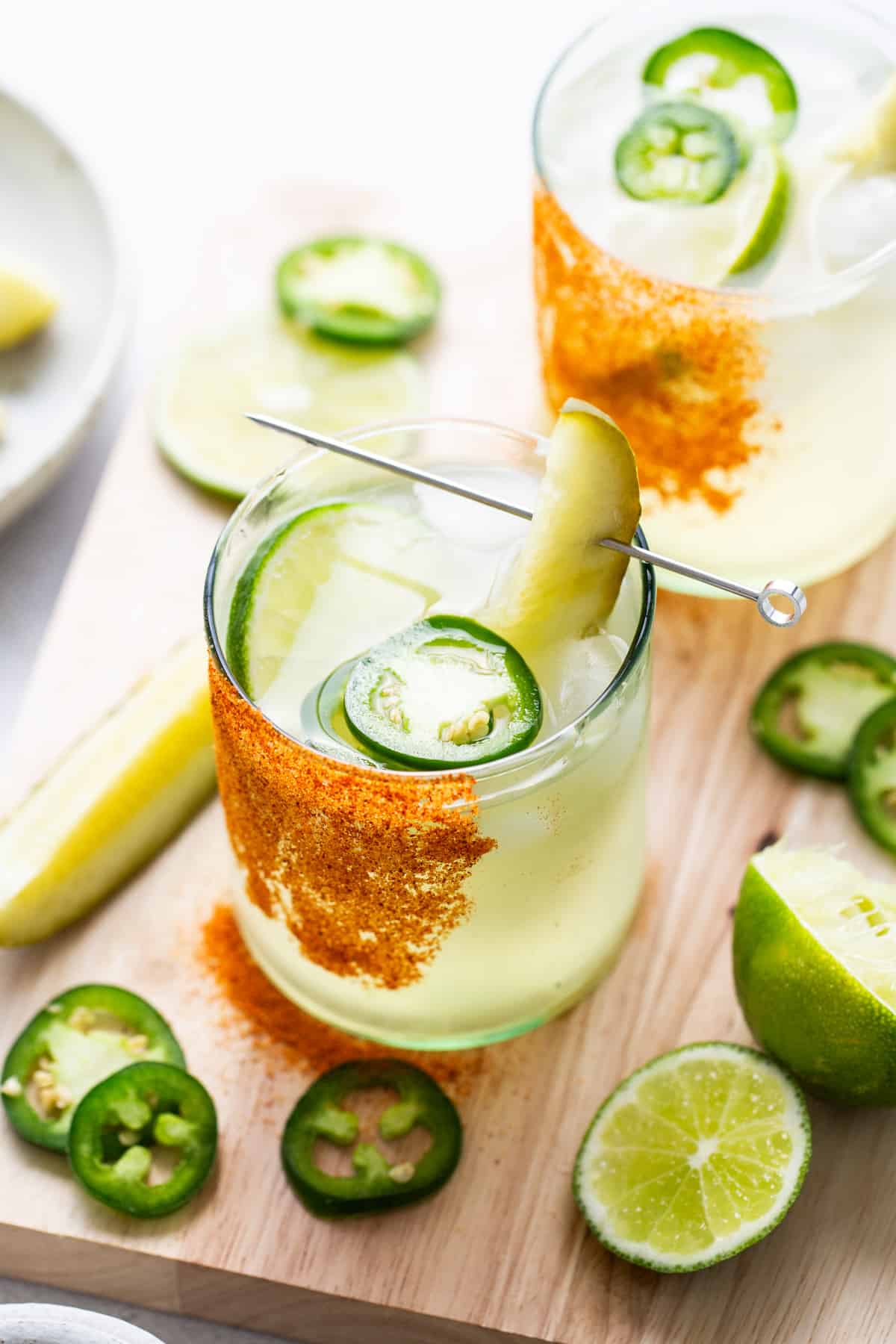 A spicy pickle margarita in a glass with pickle slices and lime wedges.