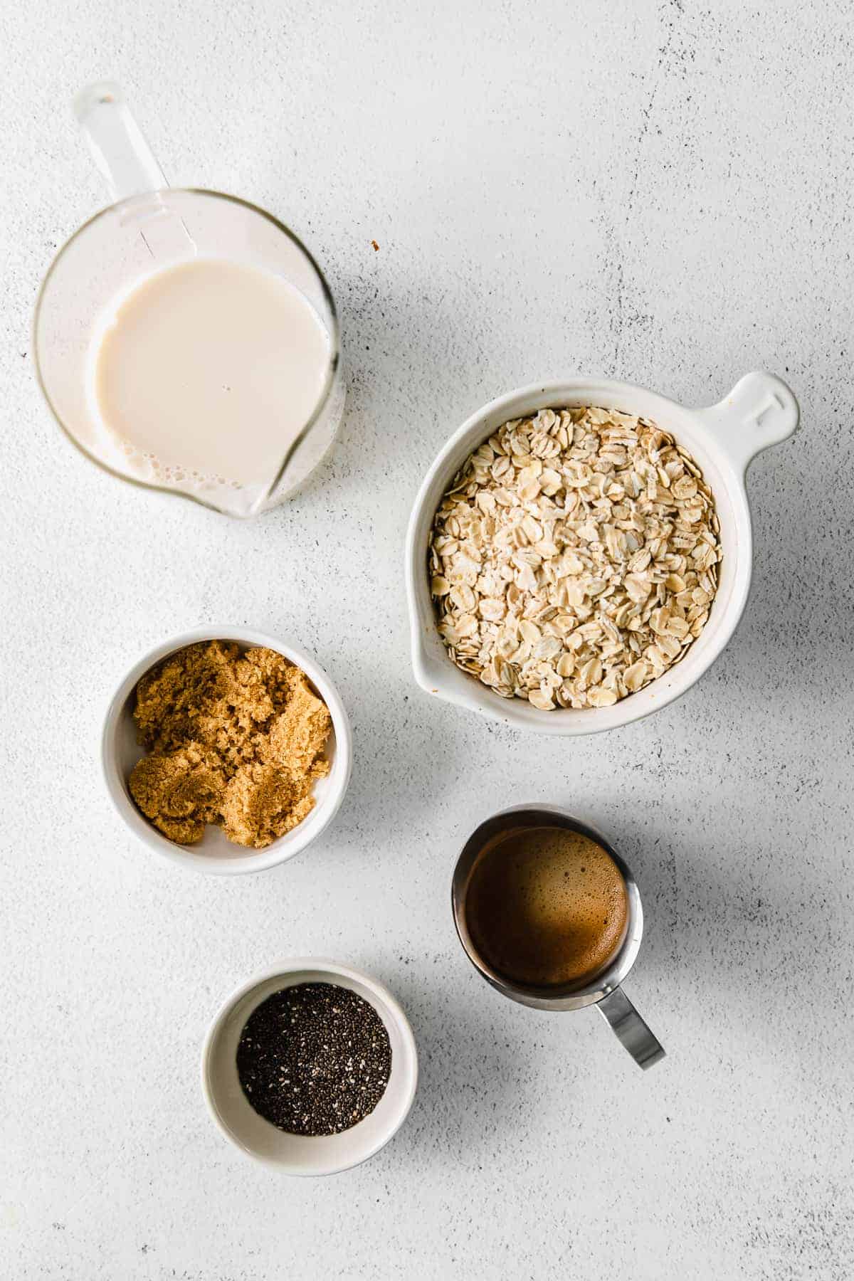 ingredients for brown sugar shaken espresso overnight oats laid out on a counter including rolled oats, brown sugar, chia seeds, almond milk, and espresso concentrate