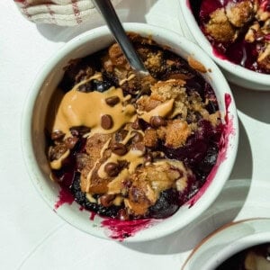 A bowl of berry crumble topped with peanut butter, chocolate chips, and a spoon resting inside.