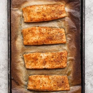 Four golden broiled salmon fillets on a parchment-lined baking sheet fresh from the oven.
