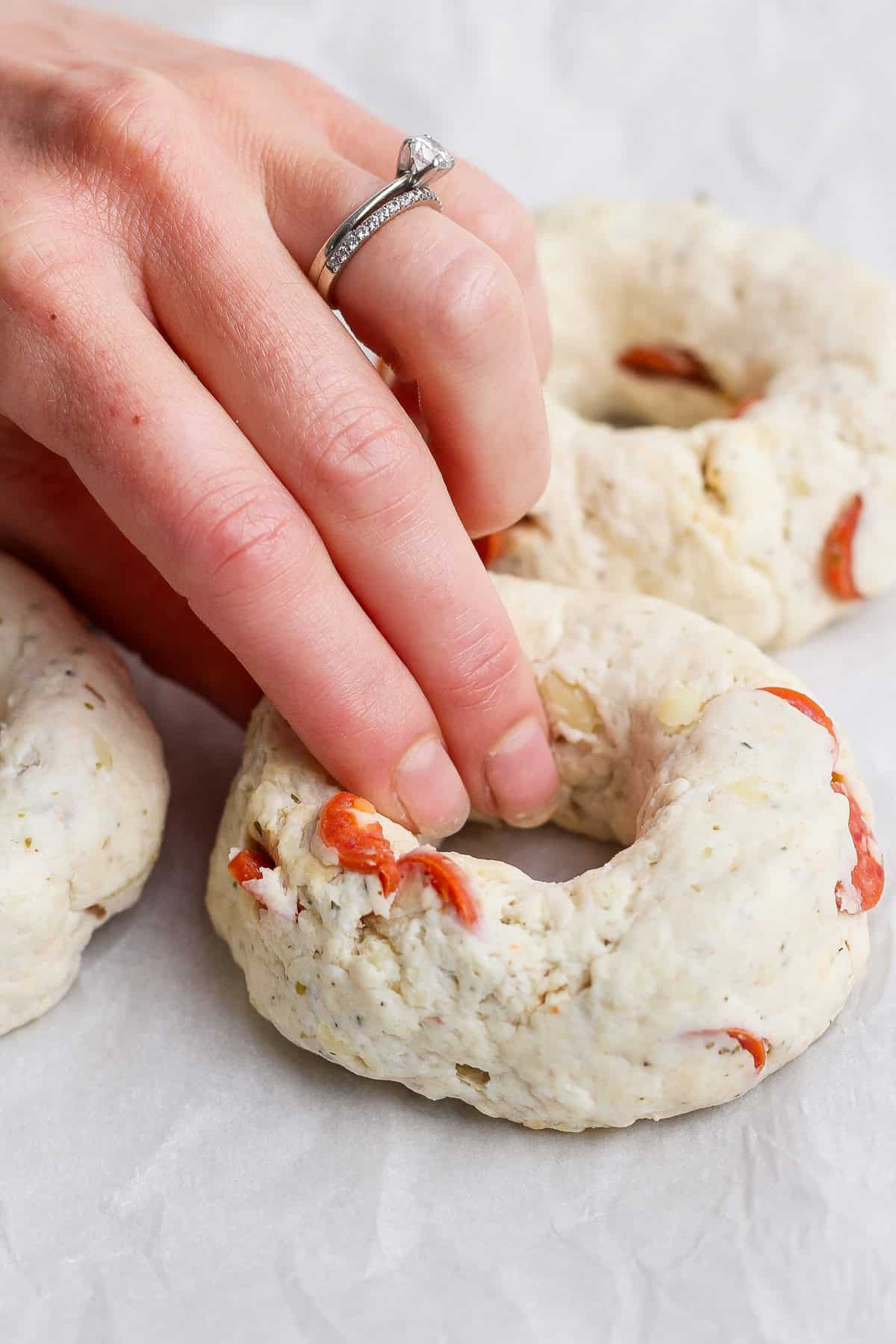 Hand shaping pizza protein bagel dough with pepperoni pieces on parchment paper
